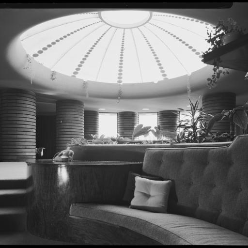 Black and white photo of a lounge with a cushion and a large skylight overhead