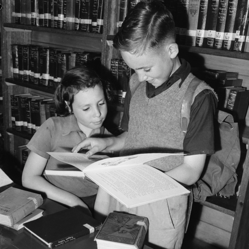 Two children reading book in front of bookcase